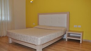 A bedroom with a bed, a nightstand, and a wall socket. - Grand White City (Velabisht)
