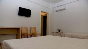 A hotel room with a bed, two chairs, a television, and an air conditioning unit. - Grand White City (Velabisht)