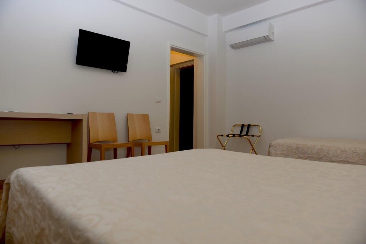 Una habitación de hotel con una cama, dos sillas, un televisor y un equipo de aire acondicionado.
