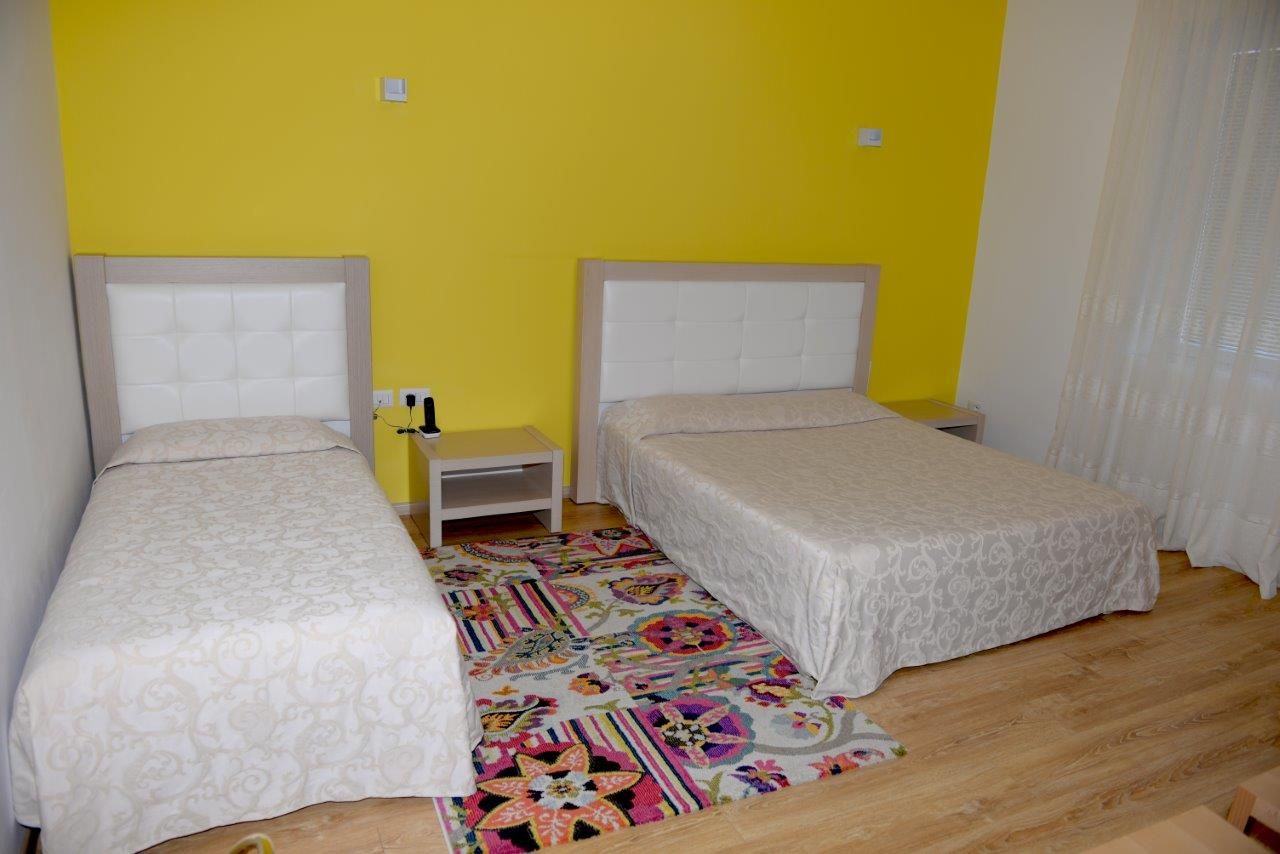 Una stanza con due letti singoli, un comodino e un tappeto colorato.