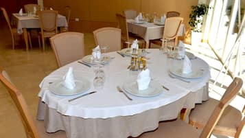 A dining area with round tables set for four, each with white tablecloths, plates, cutlery, and glassware.
