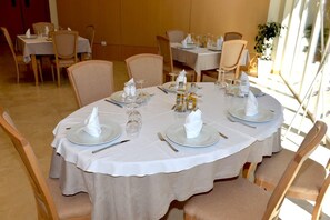 Een eetgedeelte met ronde tafels voor vier personen, elk voorzien van een witte tafelkleed, borden, bestek en glazen.