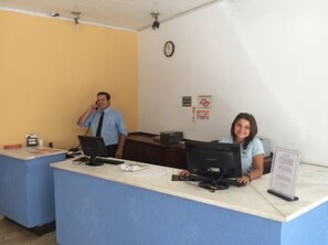A reception desk with two computer monitors, a clock on the wall, and a few papers on the counter. - Hotel Jau (Jau)