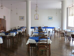 A spacious dining area with multiple tables and chairs, large windows, and hanging chandeliers. - Hotel Jau (Jau)