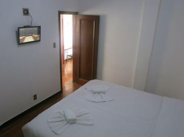 A bedroom with two beds, a wooden floor, a door leading to a hallway, and a wall-mounted TV. - Hotel Jau (Jau)