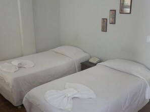 A hotel room with two single beds, each with a white bedspread and a folded towel. There is a small bedside table with a telephone and a wall-mounted light switch. - Hotel Jau (Jau)