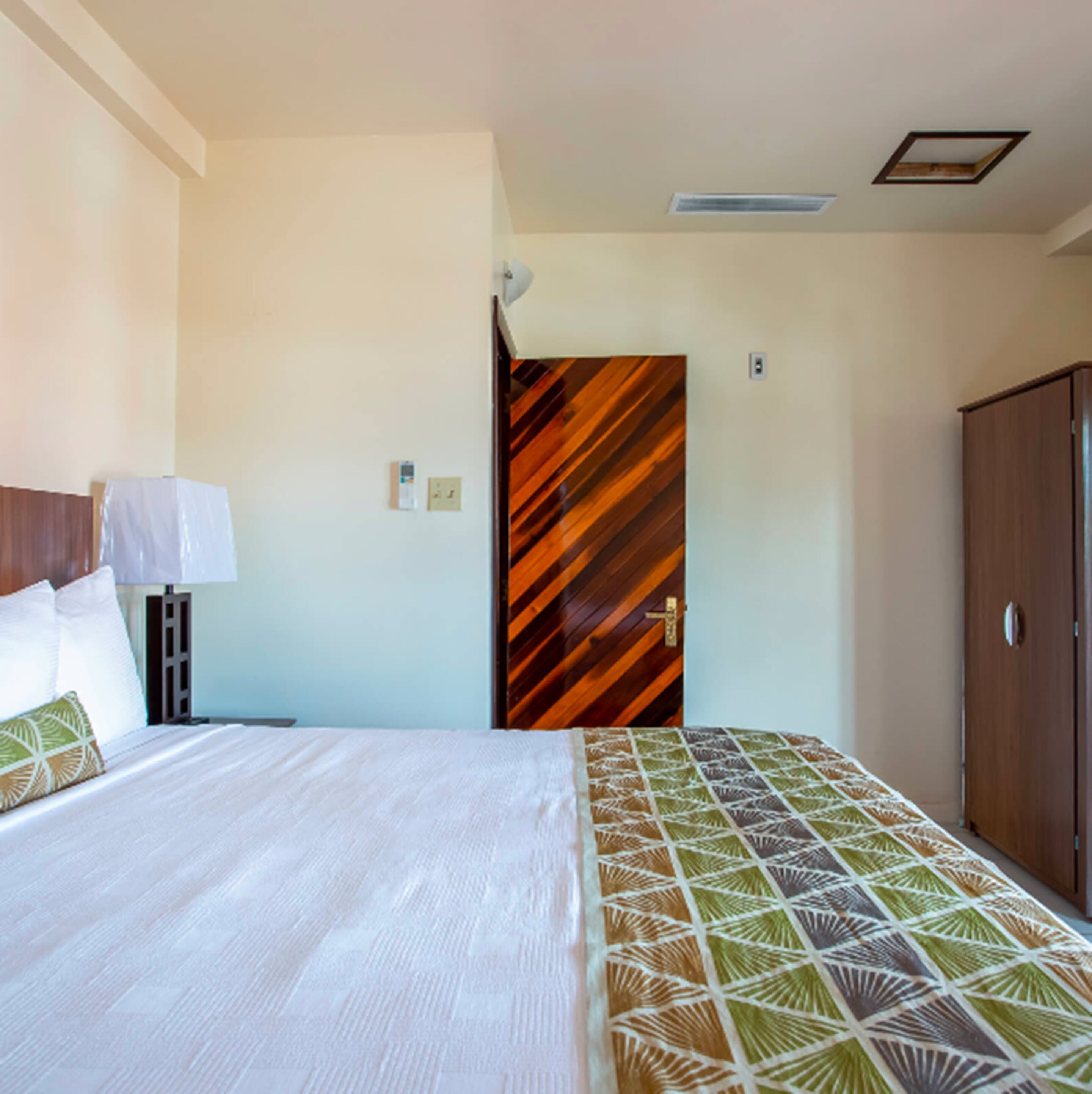 A hotel room with a bed, a wooden door, and a wardrobe.