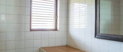 A bathroom with white tiles, a window with blinds, a sink, and a mirror.