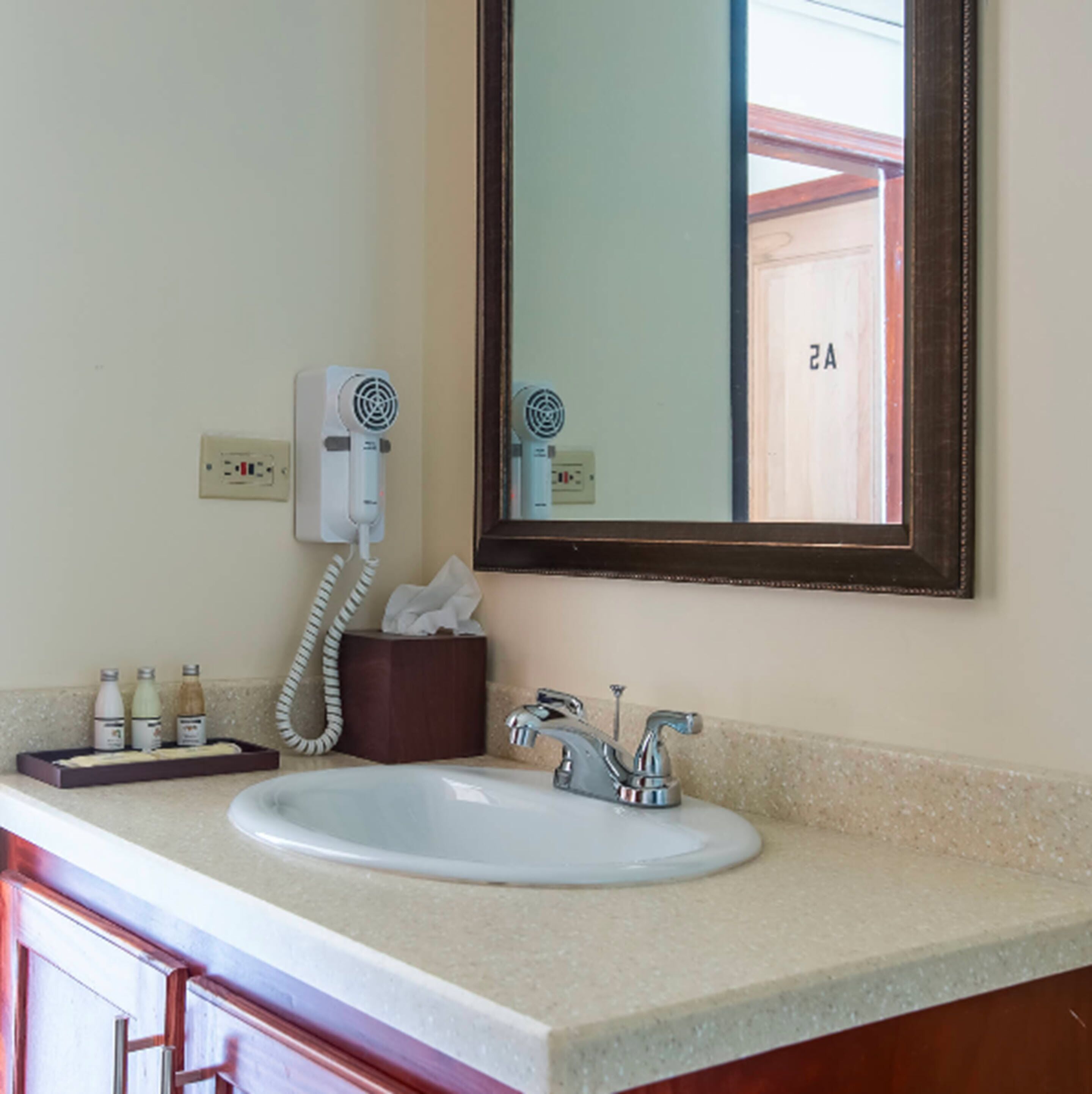 A bathroom with a sink, a mirror, a hairdryer, and a tissue box.
