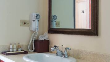 A bathroom with a sink, a mirror, a hairdryer, and a tissue box.