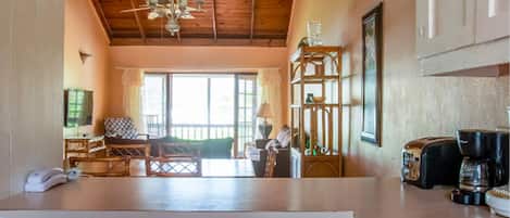 A kitchen with white cabinets, a wooden ceiling, and a view into a dining area with a table and chairs.