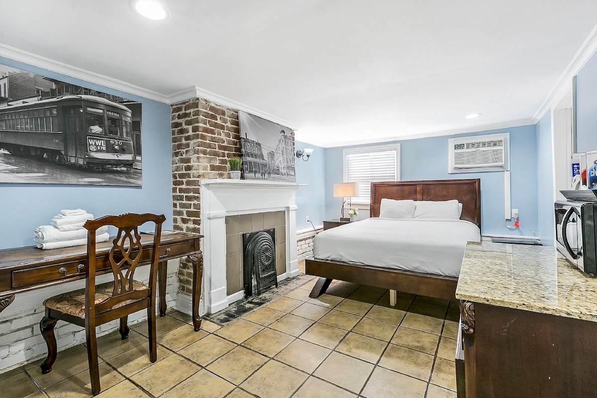 A hotel room with a bed, a desk, a chair, a fireplace, and a wall with a vintage tram picture.