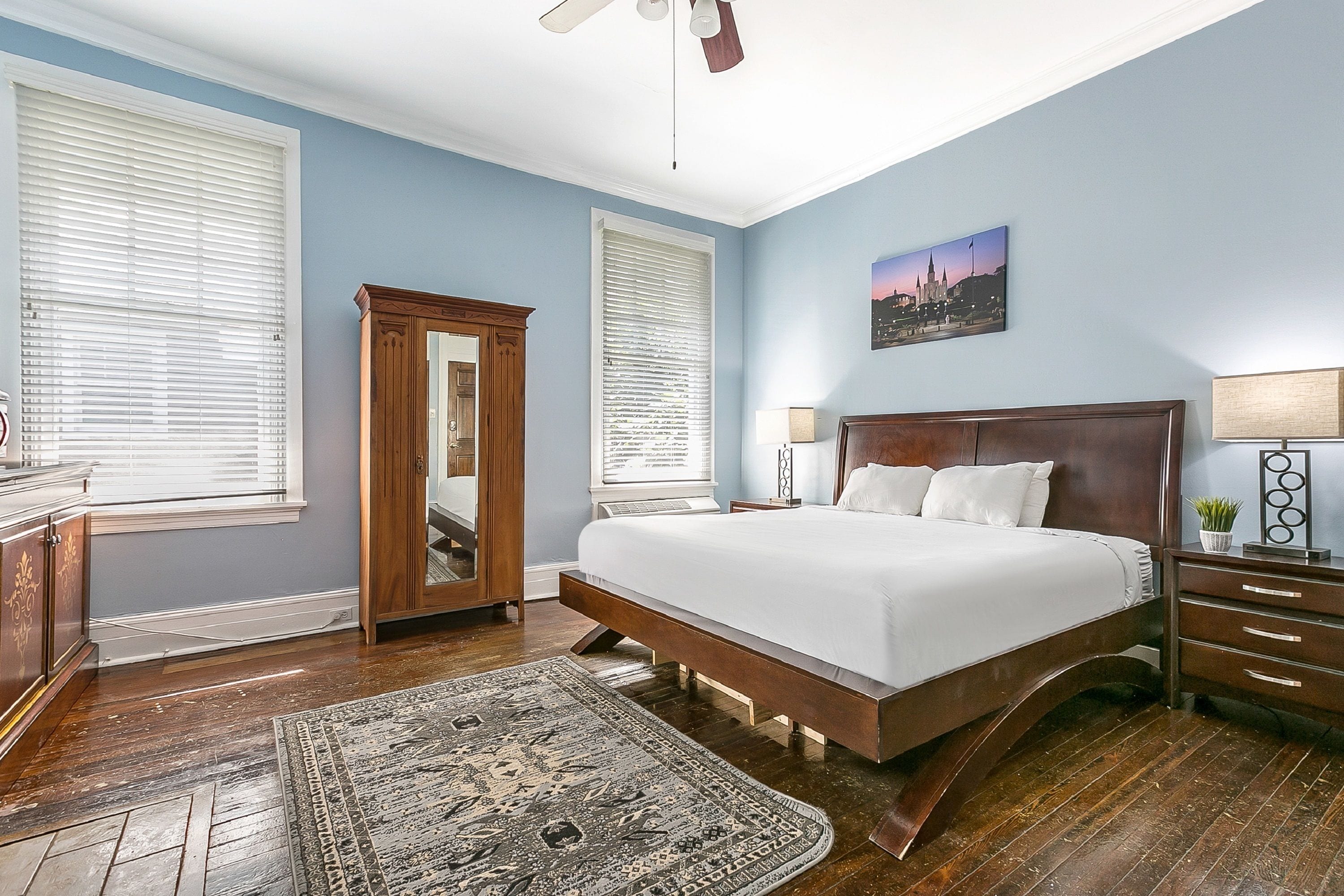 A bedroom with a large bed, wooden floor, and a ceiling fan.