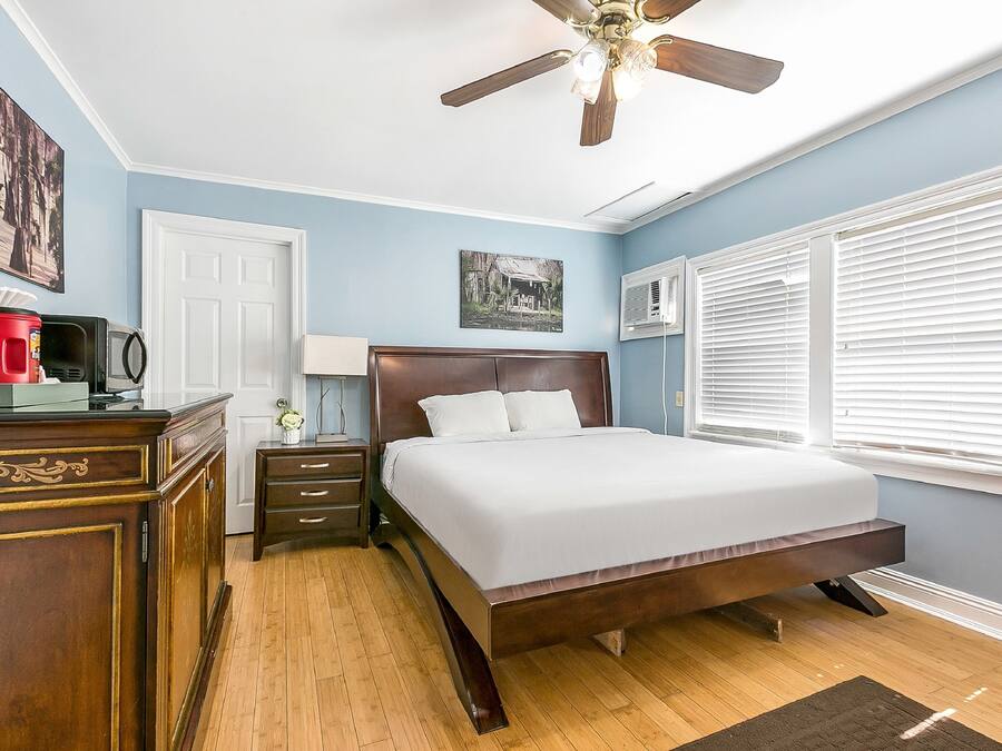 Un dormitorio con cama, ventilador de techo, cómoda, mesita de noche y ventana con persianas.