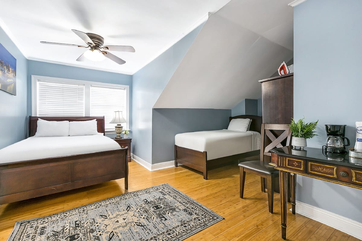 A bedroom with a bed, bedside table, lamp, and a desk with a chair.