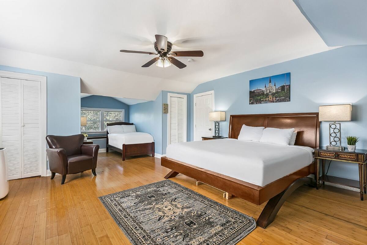 A bedroom with a large bed, a ceiling fan, a nightstand, a chair, and a window.