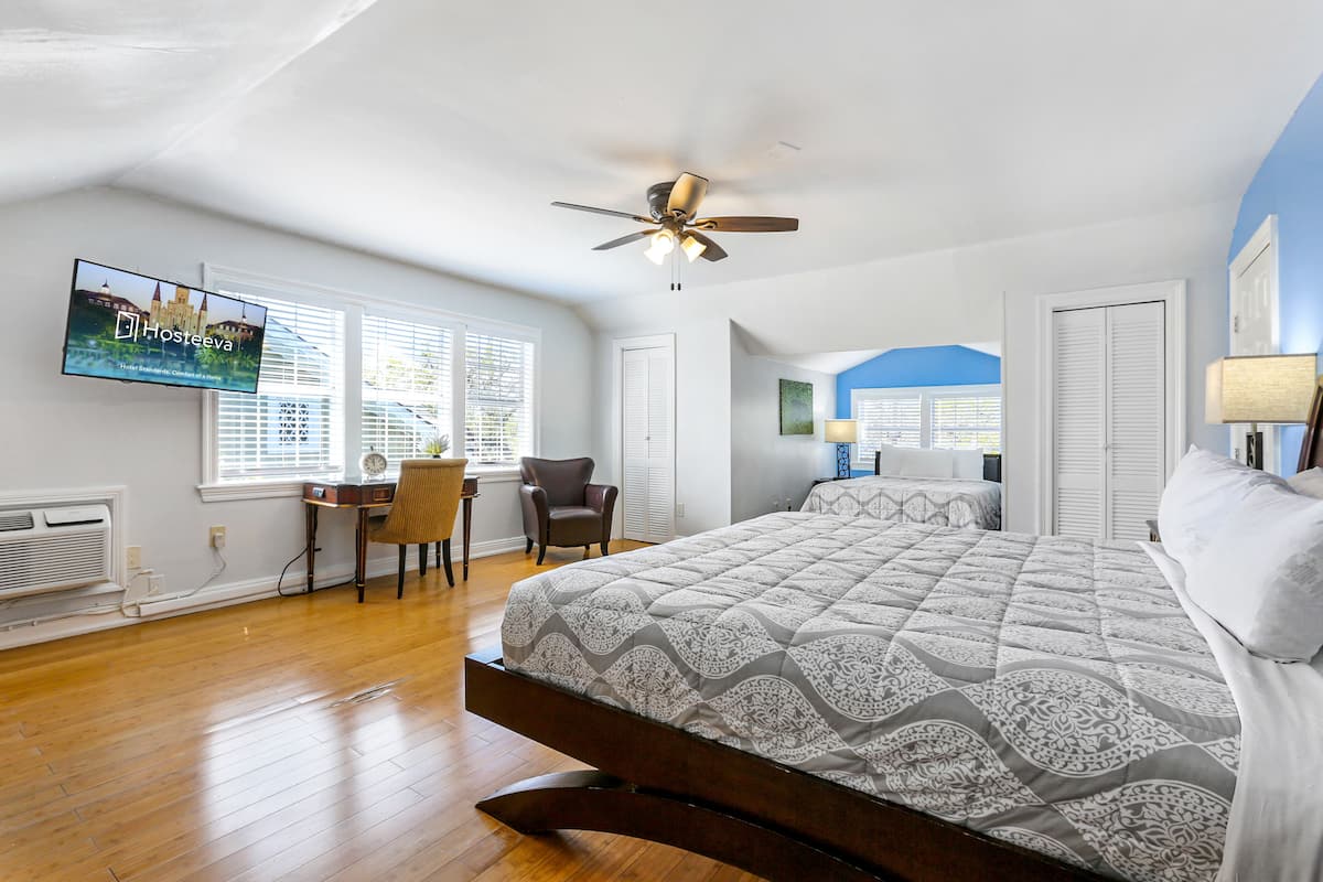 A spacious bedroom with a large bed, a ceiling fan, and a television displaying a cityscape.