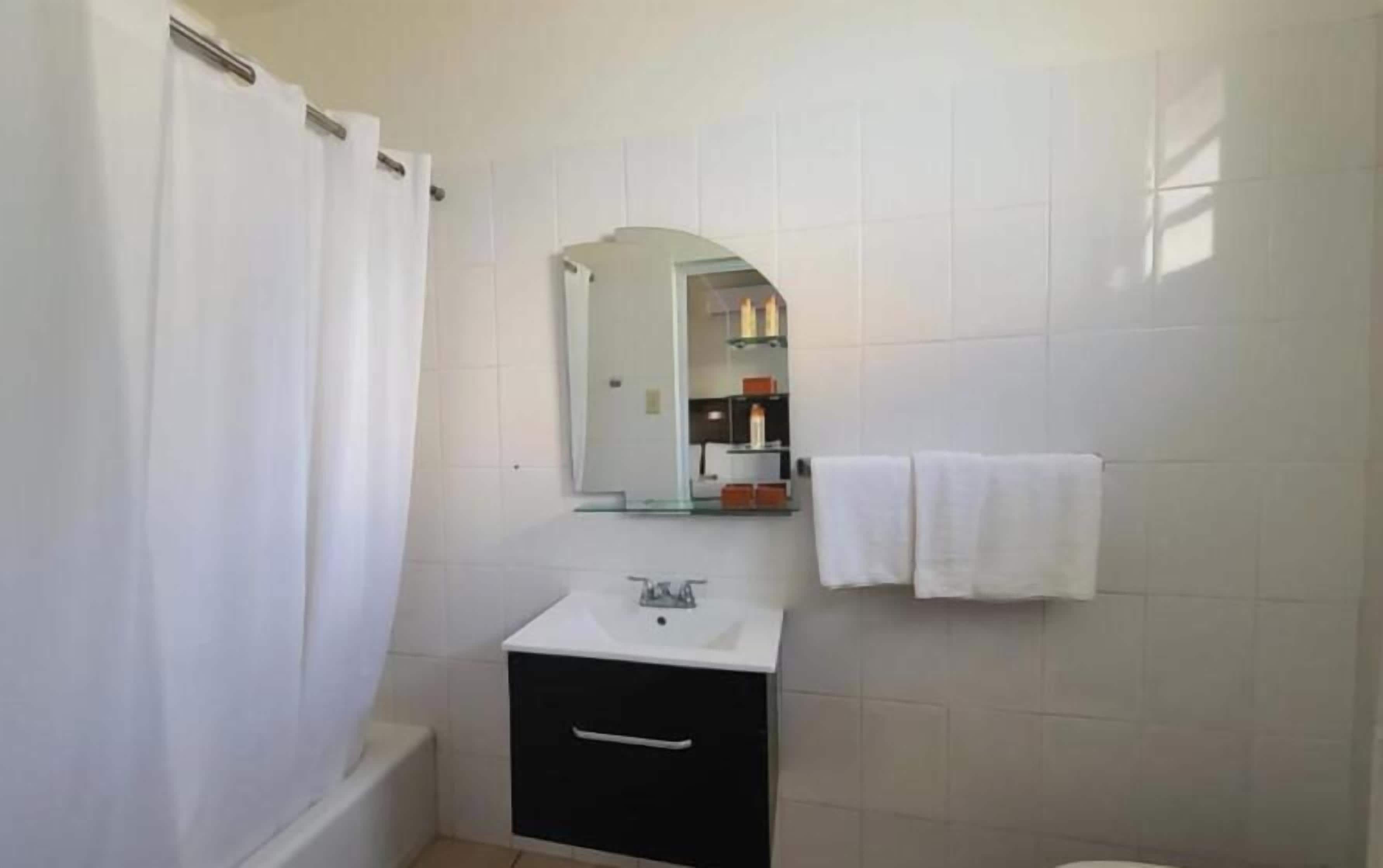 Un baño con lavamanos blanco, espejo, toallero y cortina de ducha.