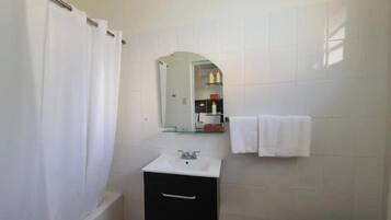 Un baño con lavamanos blanco, espejo, toallero y cortina de ducha.