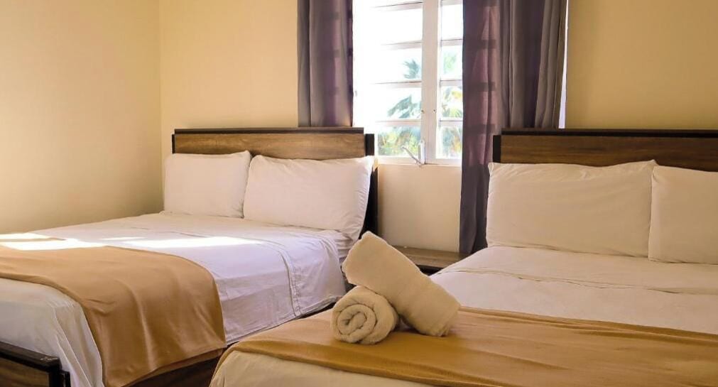 Een hotelkamer met twee bedden, elk met een houten hoofdbord, wit beddengoed en een opgerolde handdoek op het bed.