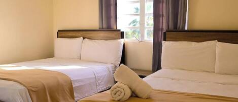Een hotelkamer met twee bedden, elk met een houten hoofdbord, wit beddengoed en een opgerolde handdoek op het bed.