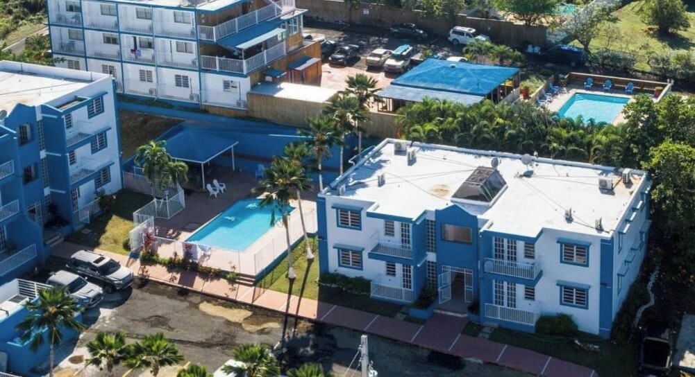 A multi-story hotel with balconies, a swimming pool, and a parking area.