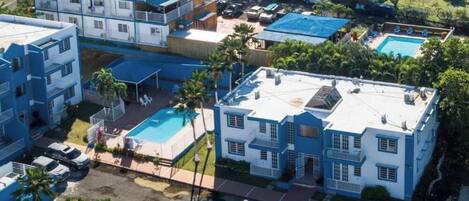 A multi-story hotel with balconies, a swimming pool, and a parking area.