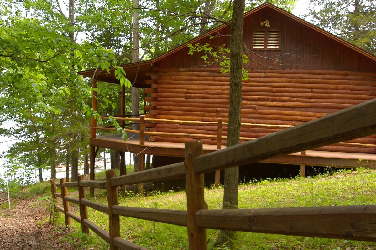 Una cabaña de madera con un porche, rodeada de árboles y una valla de madera.
