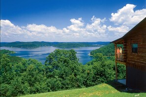 A cabin with a balcony overlooking a lake surrounded by dense forest.