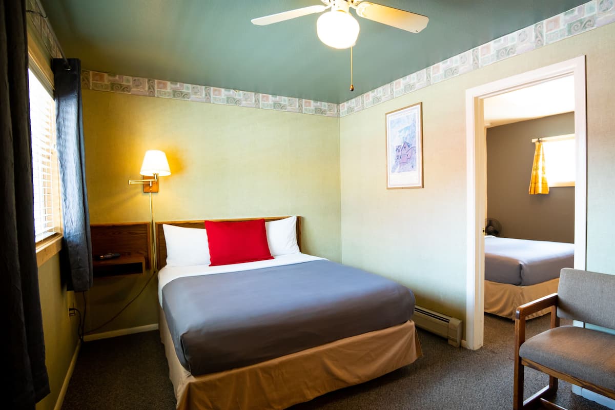 A hotel room with a bed, a chair, a desk, a lamp, and a ceiling fan.