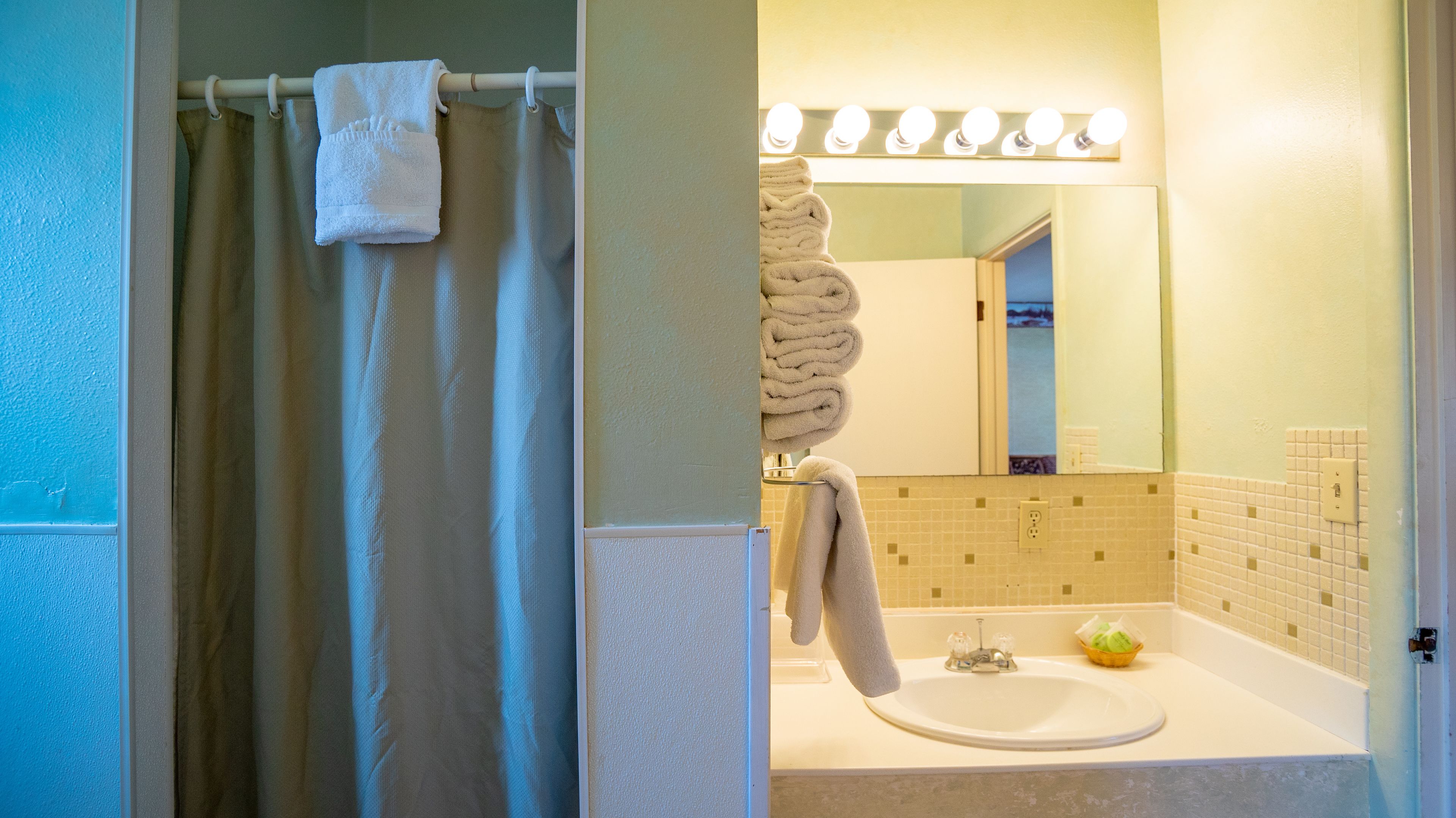 A bathroom with a shower curtain, a sink, a mirror with lights, and a towel rack.