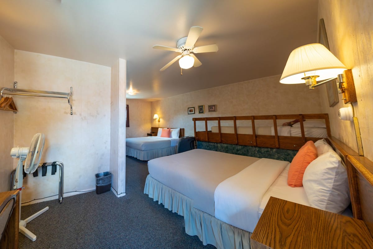 A hotel room with two beds, a ceiling fan, wall-mounted lamps, a wooden headboard, and a desk with a mirror.