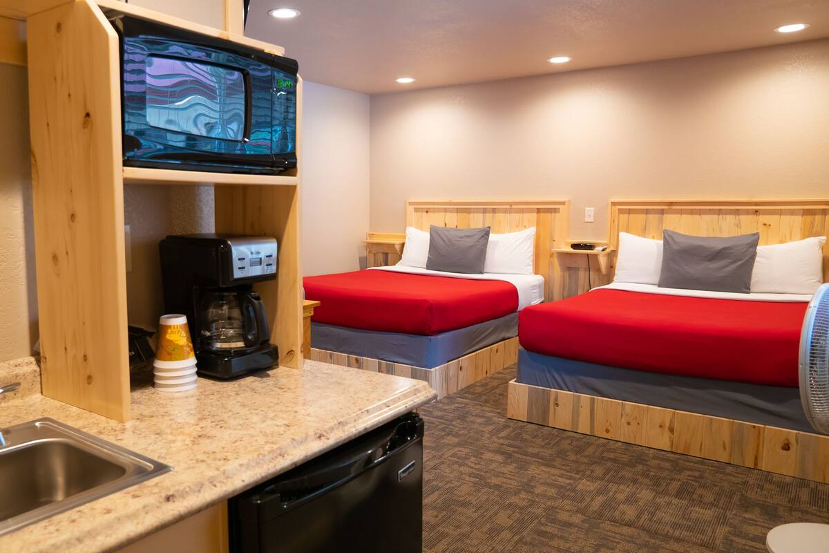 A hotel room with two beds, a sink, a coffee maker, and a television.