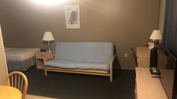 A small, dimly lit room with a single bed, a desk, a chair, and a table.