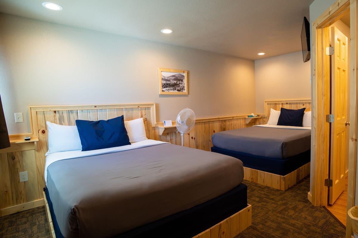 A hotel room with two beds, a wooden headboard, a wall-mounted fan, and a picture frame.