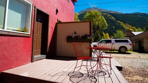 A red building with a wooden deck, a table and chairs, and a white SUV parked nearby. - Triangle Motel (Silverton)