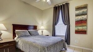 Une chambre à coucher avec un lit, des tables de chevet, un ventilateur de plafond et une fenêtre avec des rideaux.