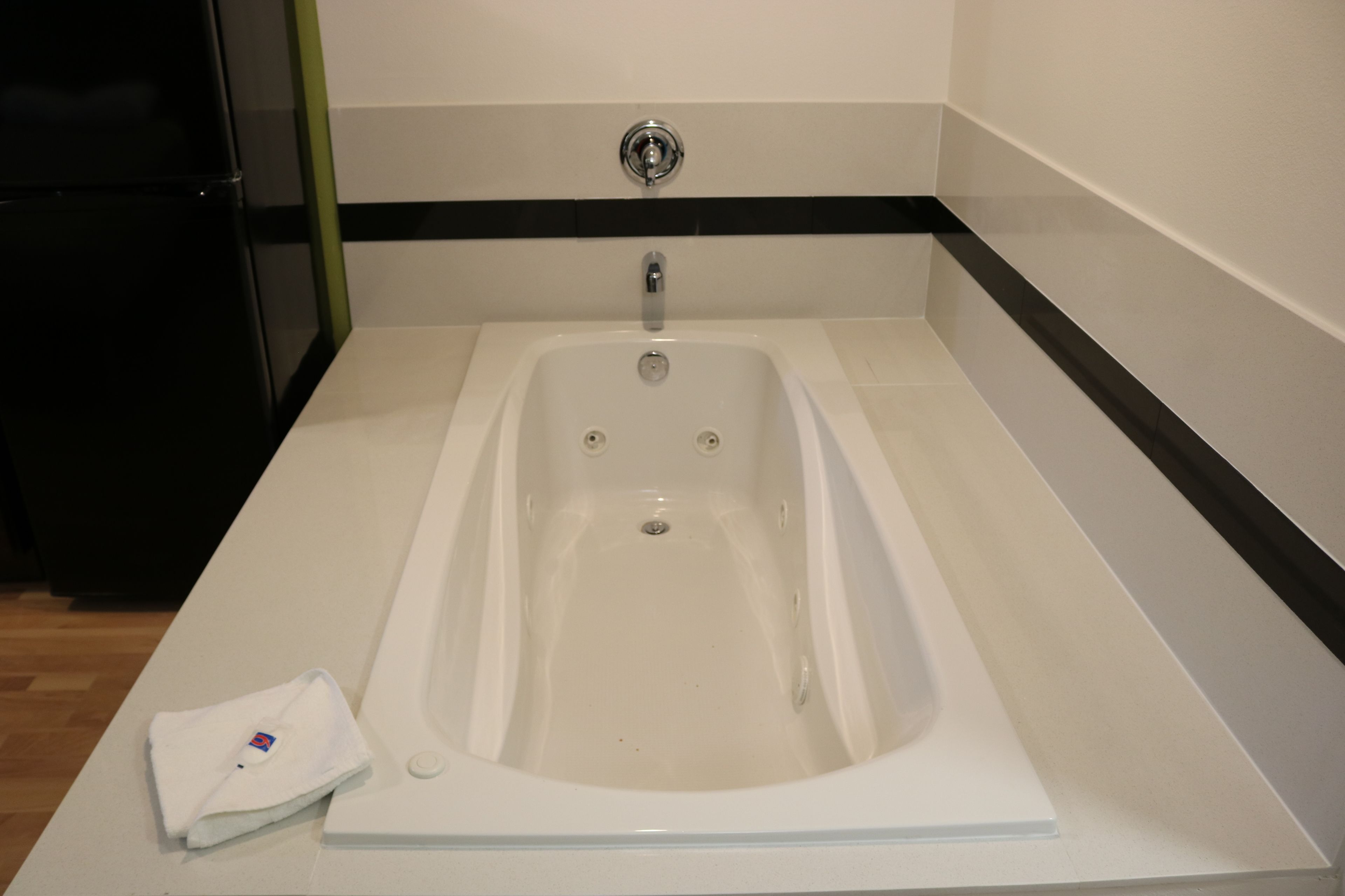 A modern bathroom with a white bathtub, a black and white striped wall, and a white towel on the counter.