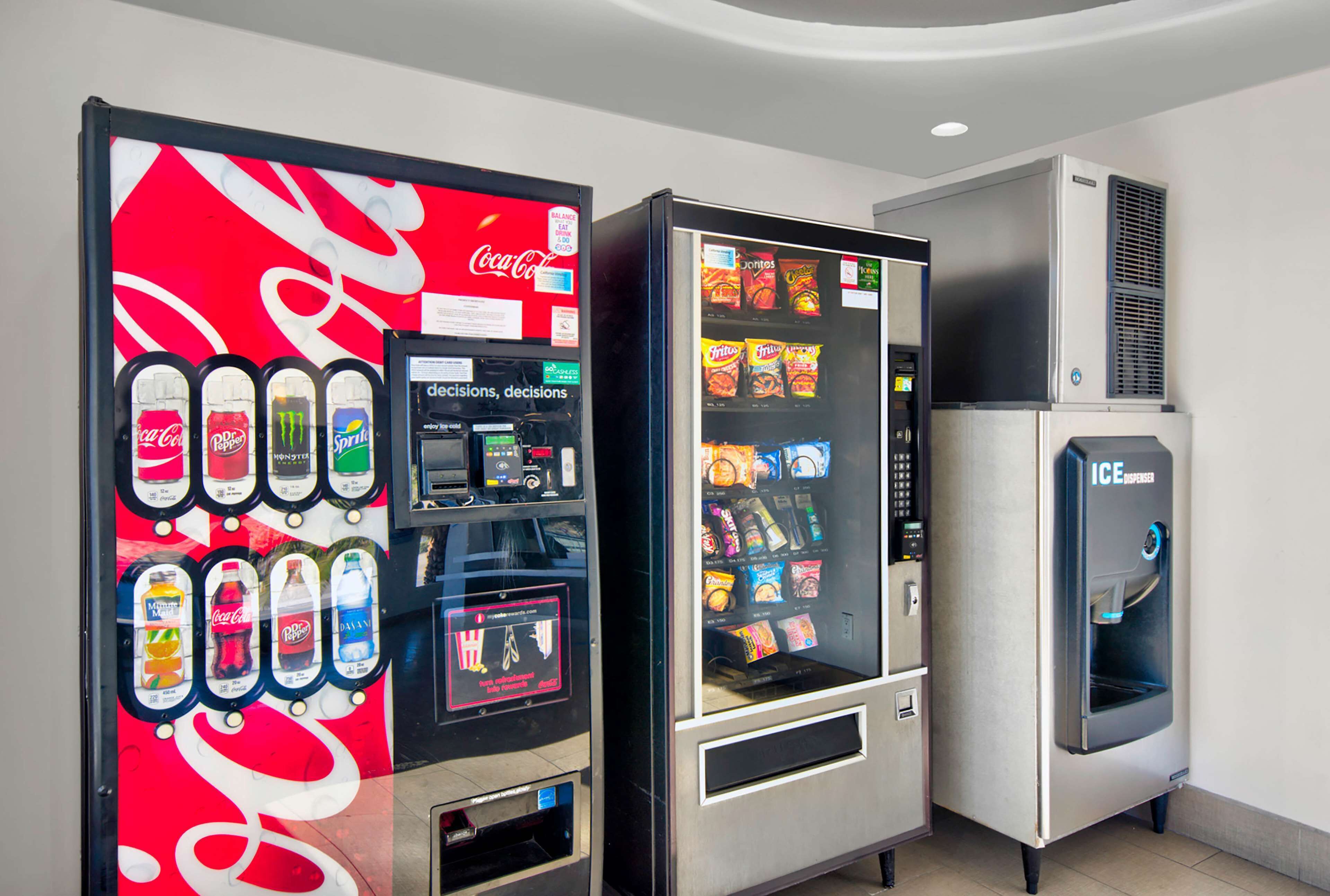 Una macchina distributrice con il logo Coca-Cola, un erogatore di bevande e una selezione di snack.