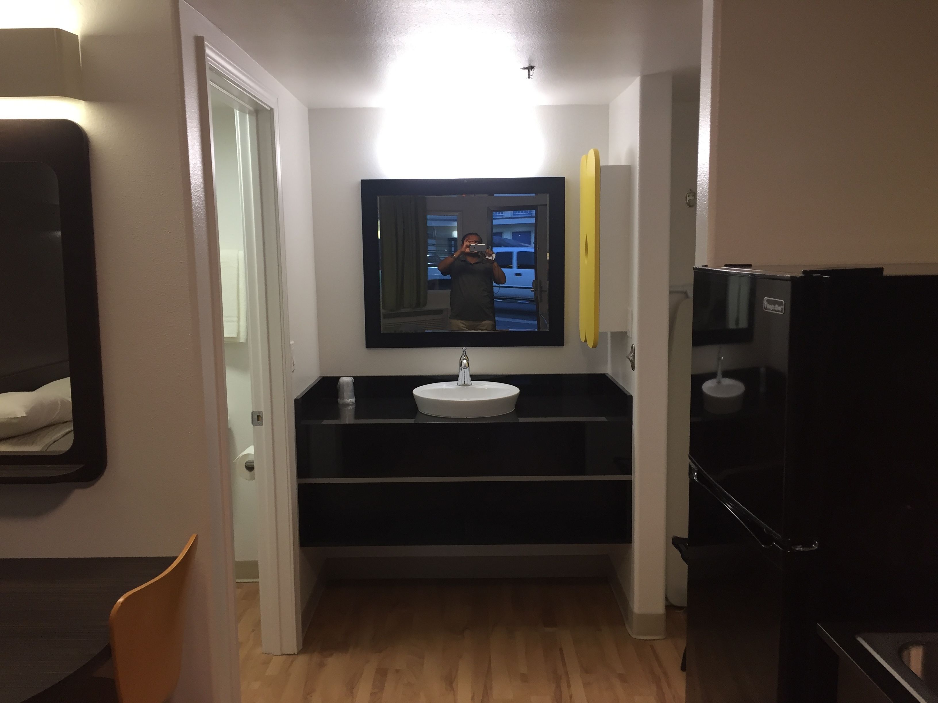 Un couloir étroit mène à une salle de bain équipée d’un lavabo, d’un miroir et de toilettes.
