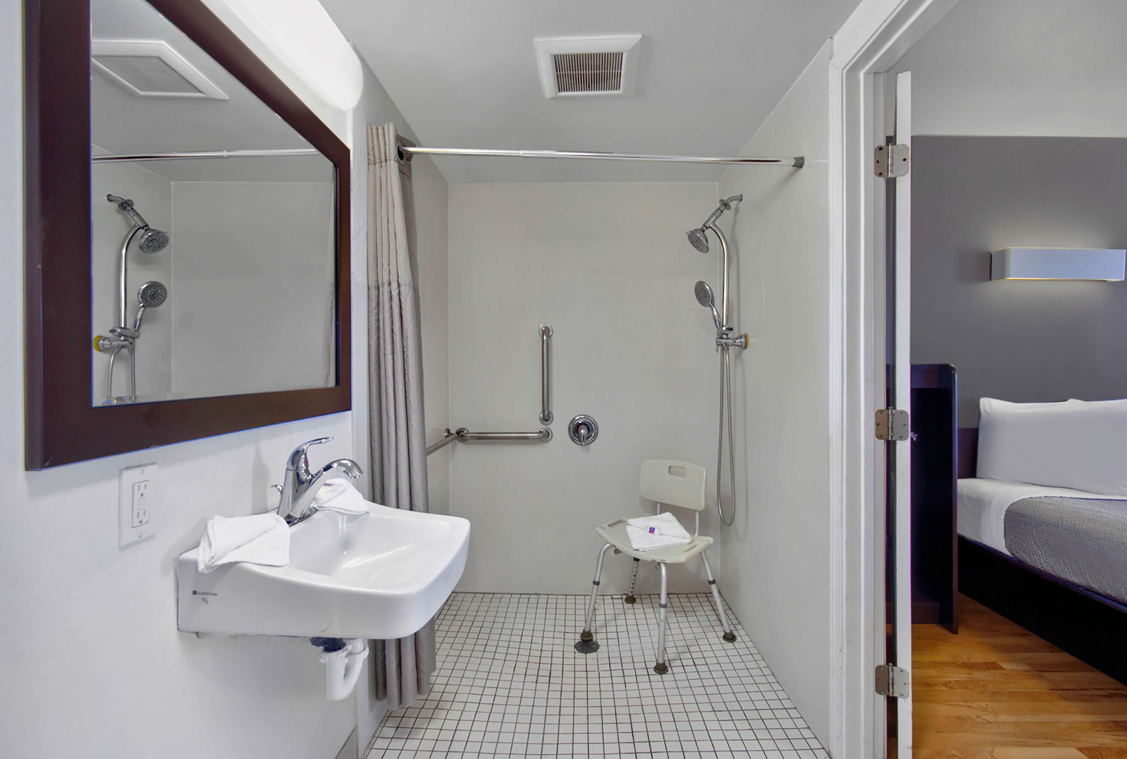 A modern bathroom with a shower, a sink, and a wheelchair-accessible chair.