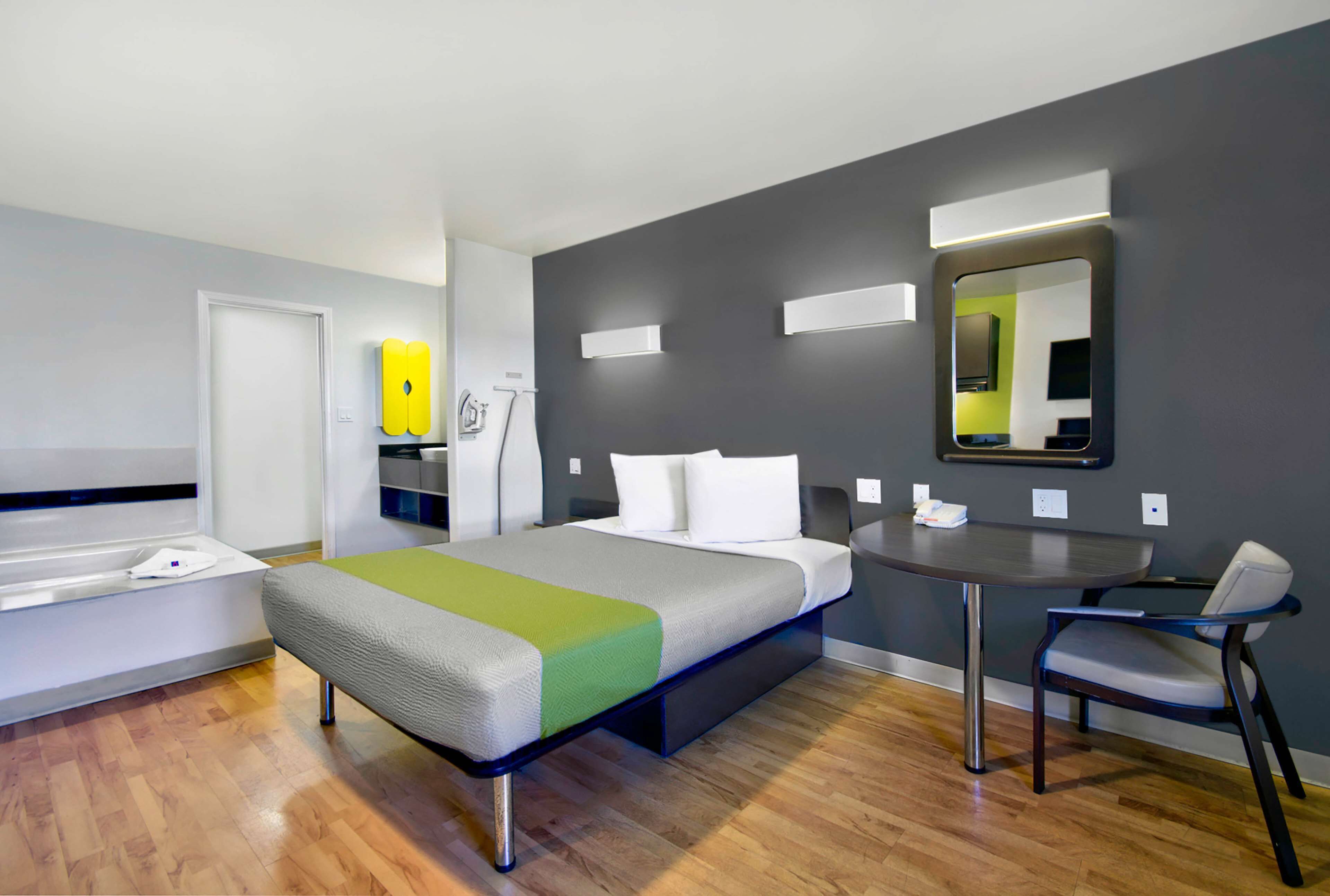 Una habitación de hotel moderna con una cama, un escritorio, una silla, un espejo y un espacio para el baño.
