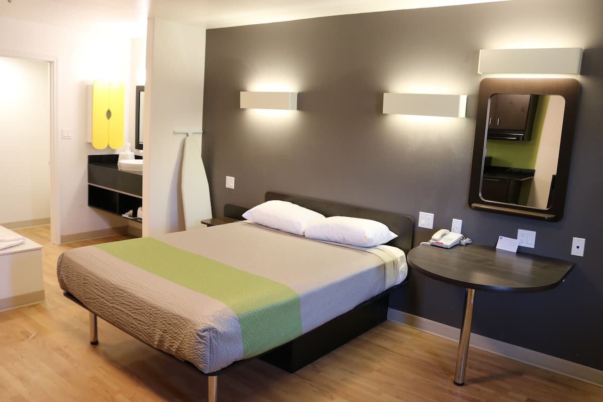 A hotel room with a bed, bedside table, and a mirror.