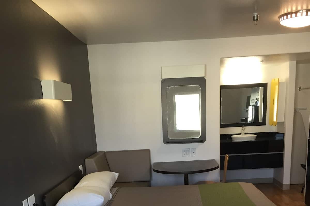 A hotel room with two beds, a small table, a chair, a desk, a mirror, and a window.