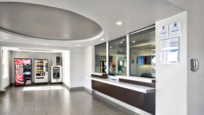 A modern reception area with a counter, vending machines, and a large window. - Studio 6 Victorville - Apple Valley (Victorville)
