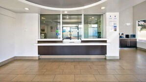 A modern reception area with a curved ceiling, a glass partition, and a counter. - Studio 6 Victorville - Apple Valley (Victorville)