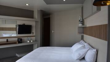Una habitación de hotel moderna con una cama grande, un televisor de pantalla plana montado en la pared, una cafetera y un estante con botellas.