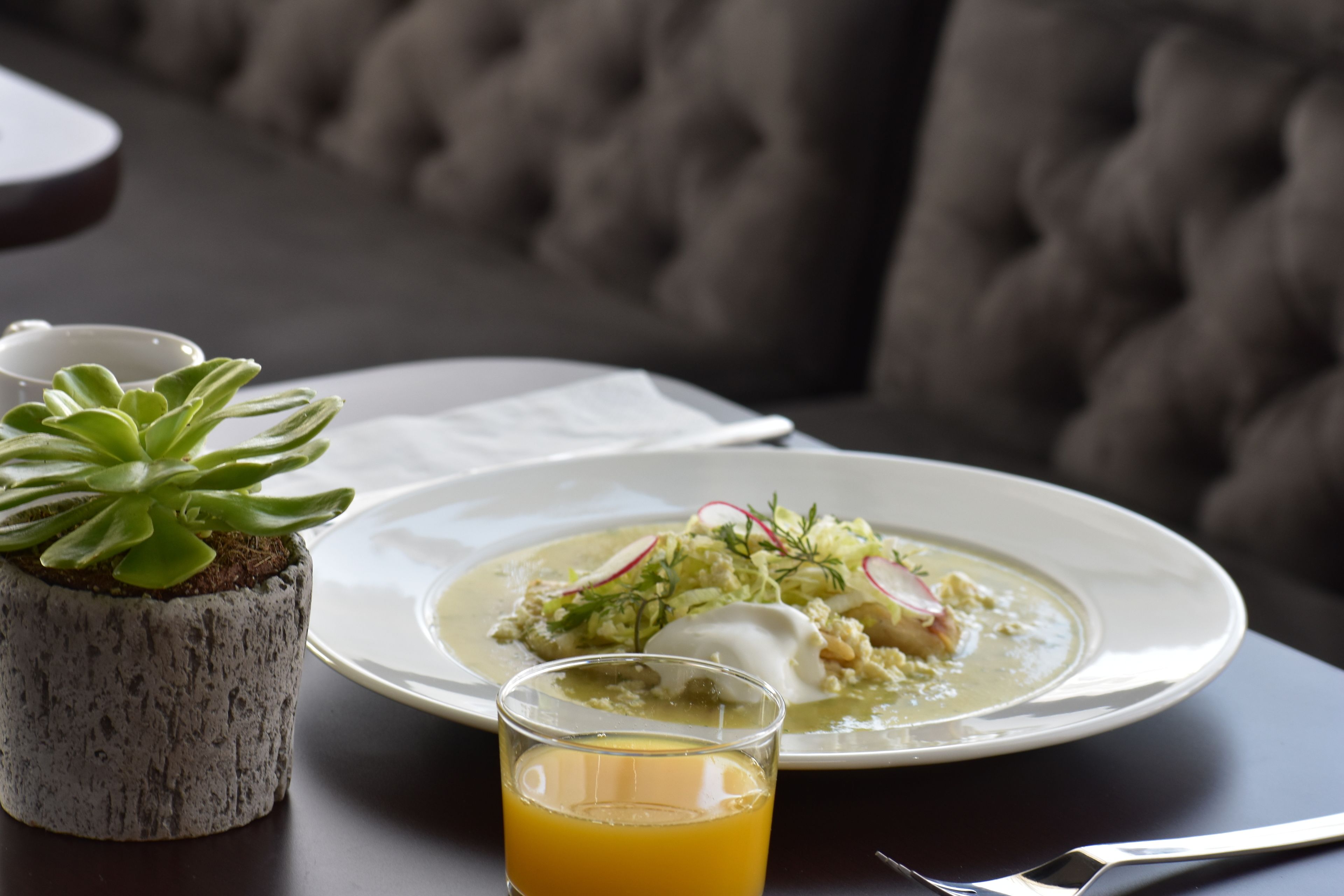 Una mesa de comedor con un plato de comida, un vaso de jugo de naranja y una pequeña planta en maceta.
