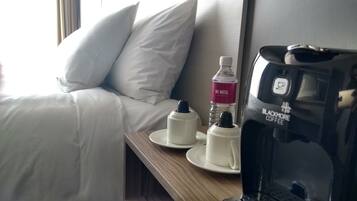 Une chambre d’hôtel avec un lit, des oreillers, une table de chevet avec une bouteille d’eau, une machine à café et une assiette.