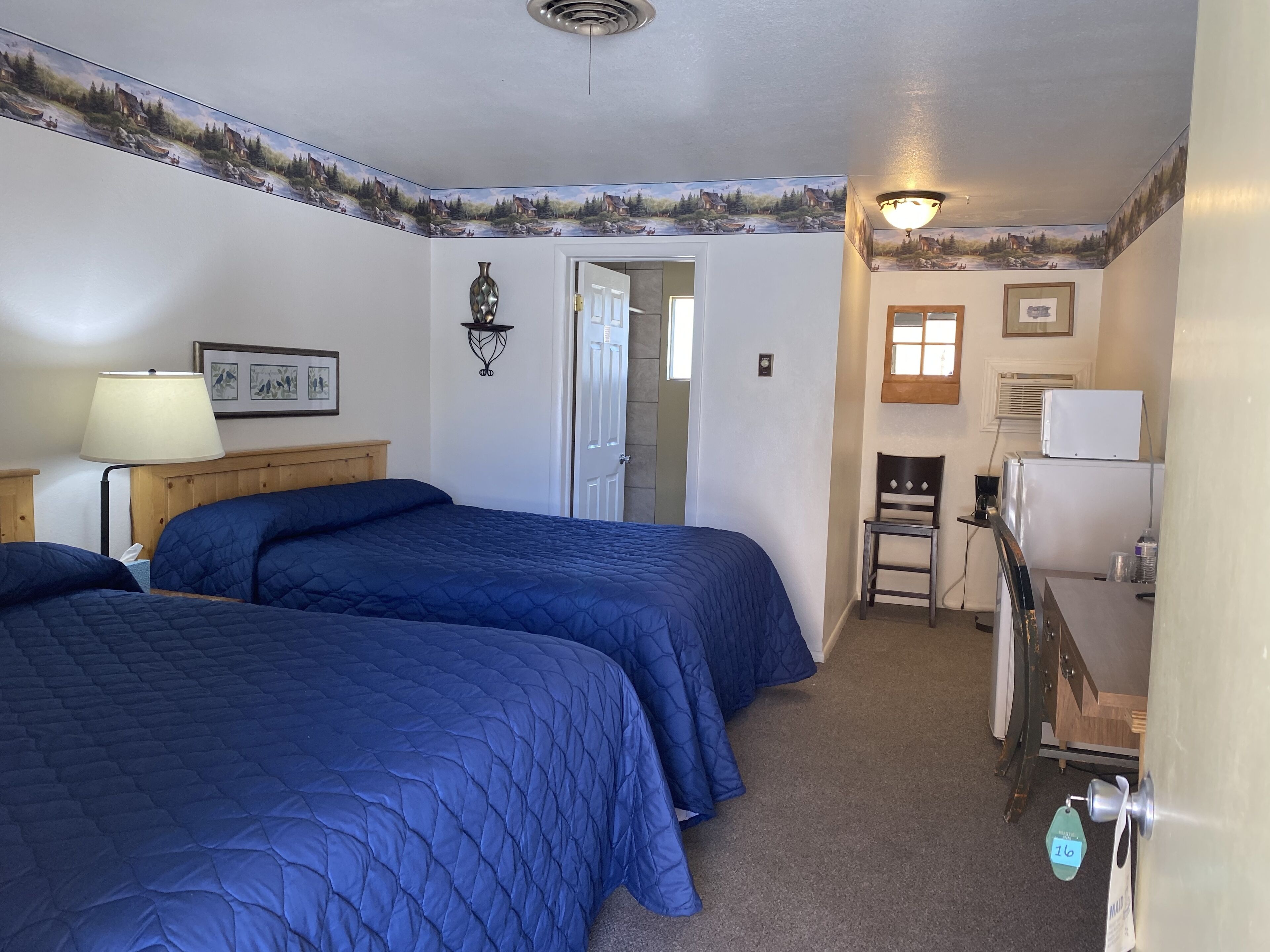 Une chambre avec deux lits, un bureau, une chaise, une lampe et un réfrigérateur.